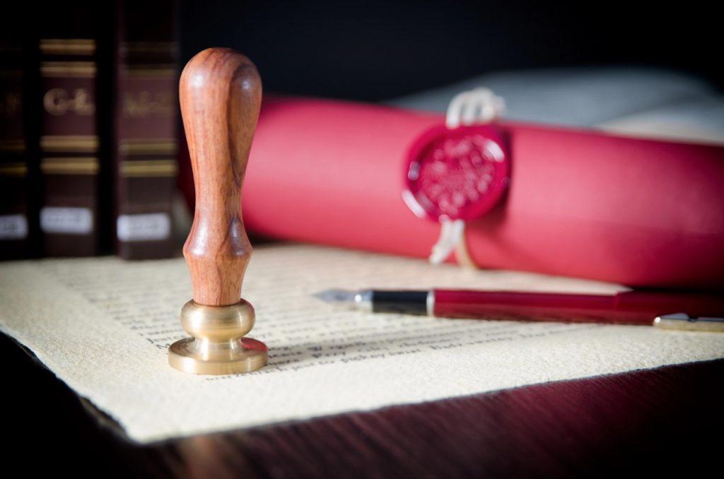 A wooden stamp rests on parchment beside a red scroll and pen